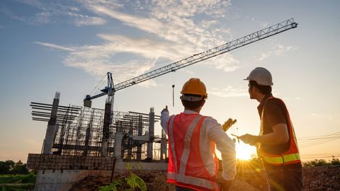 Two construction workers in hard hats at a site with a crane at sunset