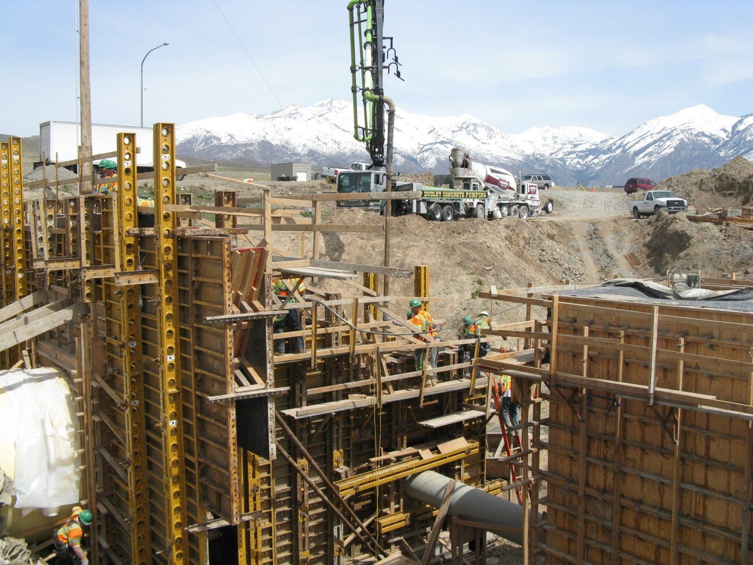 Construction site with workers and concrete forms, backed by snowy mountains