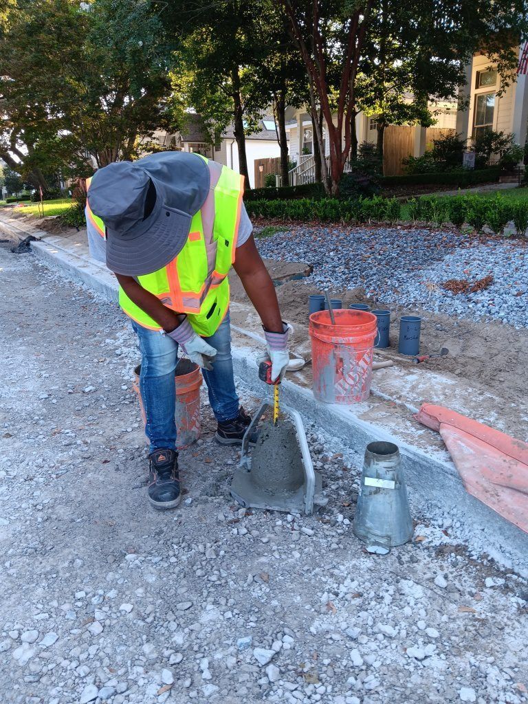 Worker in neon vest pouring concrete at a gravel roadside construction site