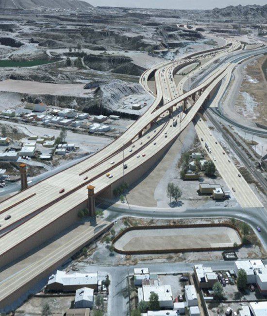 Aerial view of a highway interchange with overpasses crossing a dry, rocky landscape near small buildings.