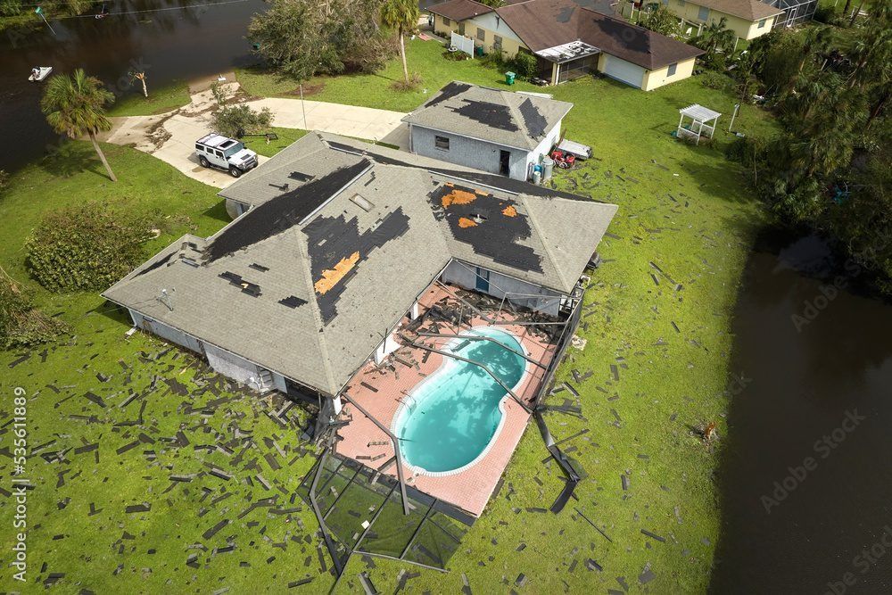 Aerial view of a suburban house with a backyard pool and patio, surrounded by green lawn and trees