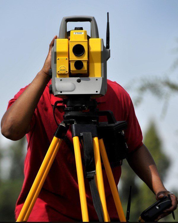 Surveyor using a yellow tripod-mounted theodolite outdoors