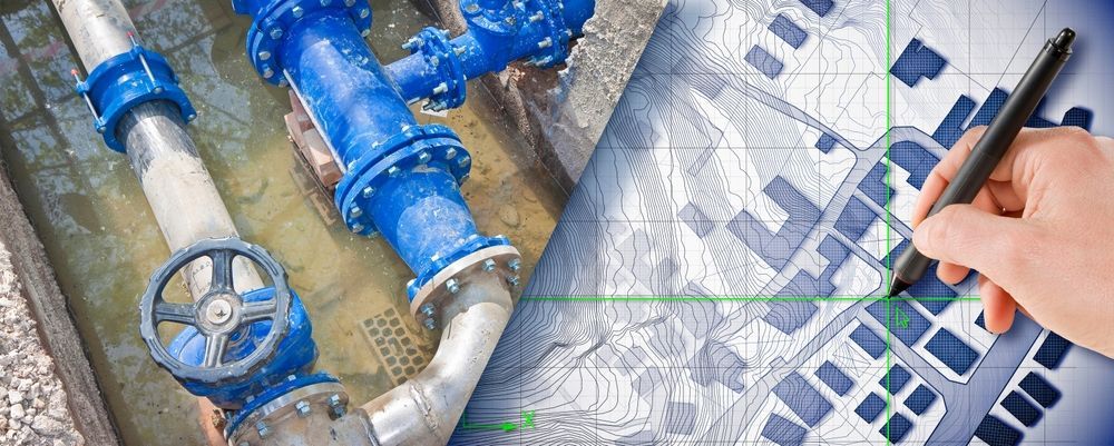 Hand holding pen over blueprint beside blue industrial pipes and valves