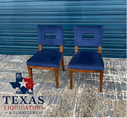 Two blue upholstered chairs with wooden legs on a weathered floor before a blue metal wall.