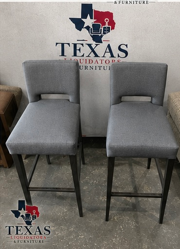 Two gray upholstered barstools in front of a Texas Furniture logo backdrop