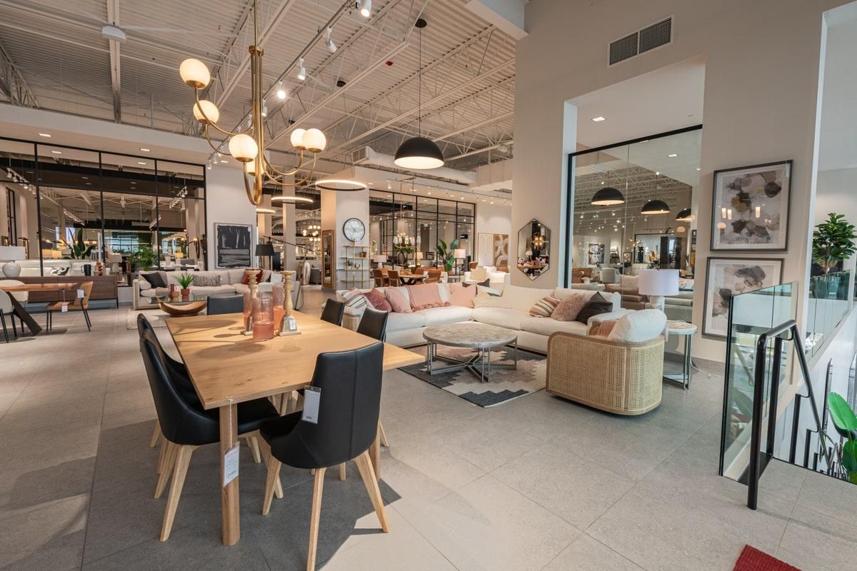 Modern furniture showroom with dining table, sofas, lamps, and mirrors in a bright open showroom