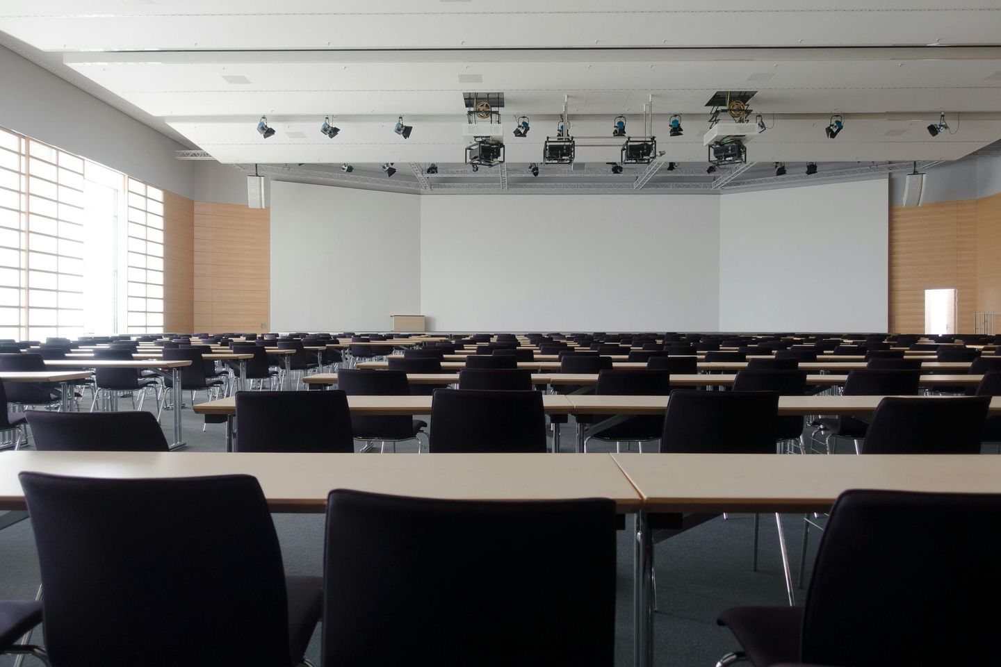 Empty conference room with rows of tables and chairs facing a blank screen.