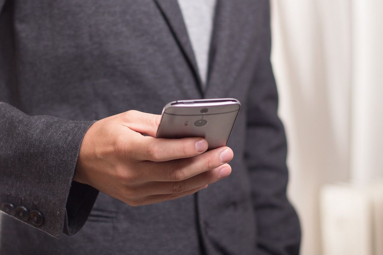 Person in a dark suit holding a smartphone, blurred background.