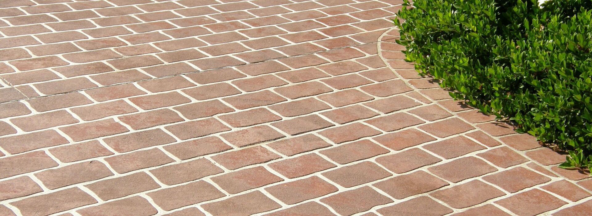 Decorative brick-patterned concrete driveway curving alongside neatly trimmed green bushes.