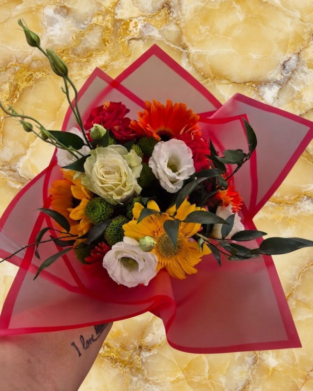 Bouquet di fiori misti avvolto in carta rossa e rosa, su uno sfondo di marmo