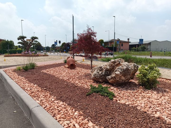 Spartitraffico alberato lungo la strada, con ghiaia rossa, massi, alberelli e arbusti