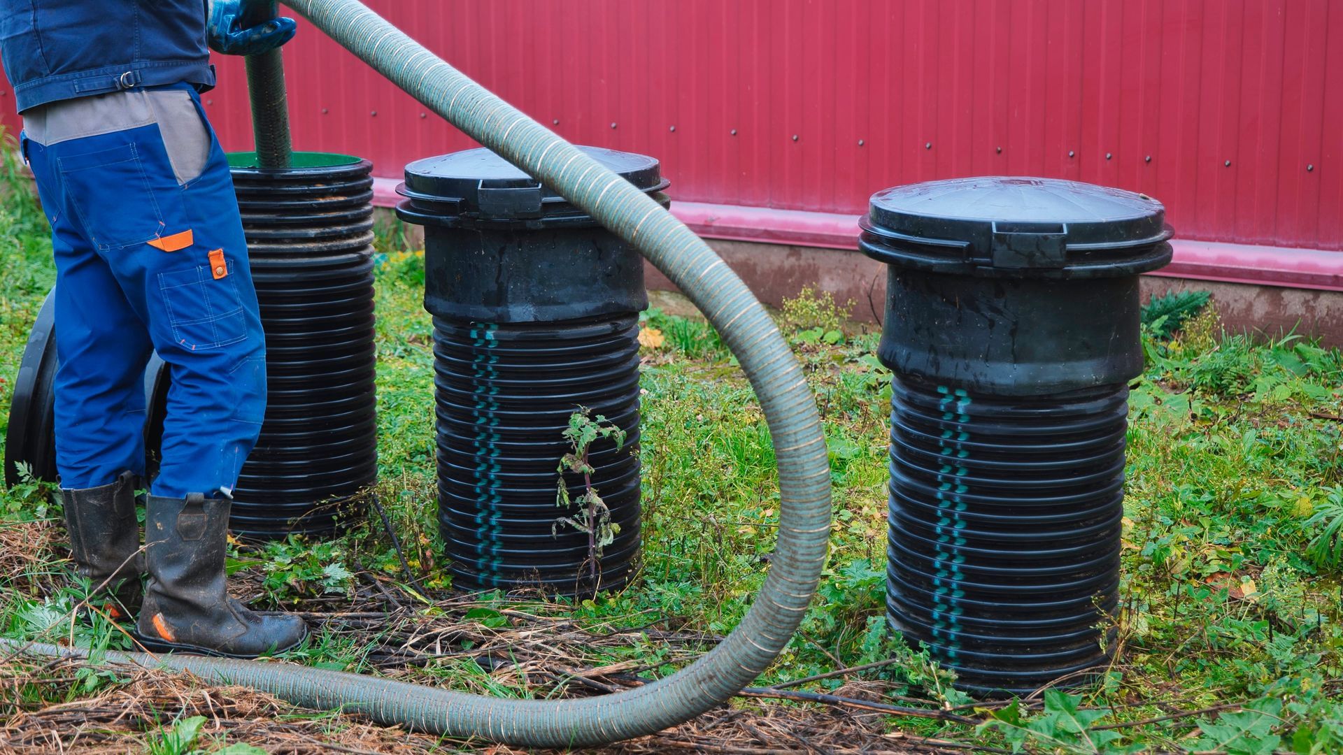 Worker operating a vacuum hose to clean or service underground septic or drainage tanks.