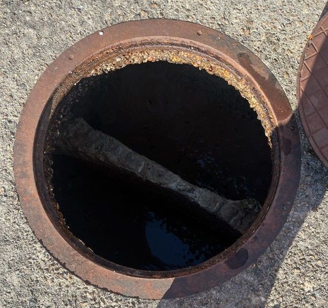 Open sewer manhole with rusted metal frame.