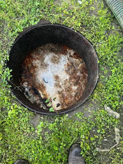 Open septic tank with brown sludge, surrounded by green grass.