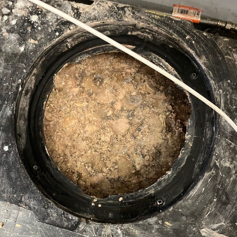 Black circular opening filled with light brown, solidified material, surrounded by a black plastic rim.