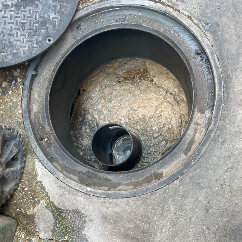 Open manhole with a metal pipe visible inside, surrounded by concrete.z