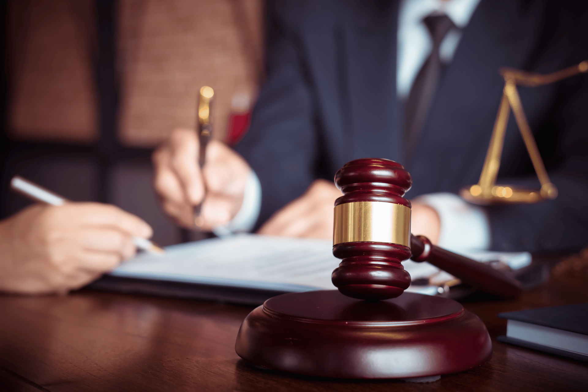 Lawyer writing at desk beside a judge’s gavel and scales of justice