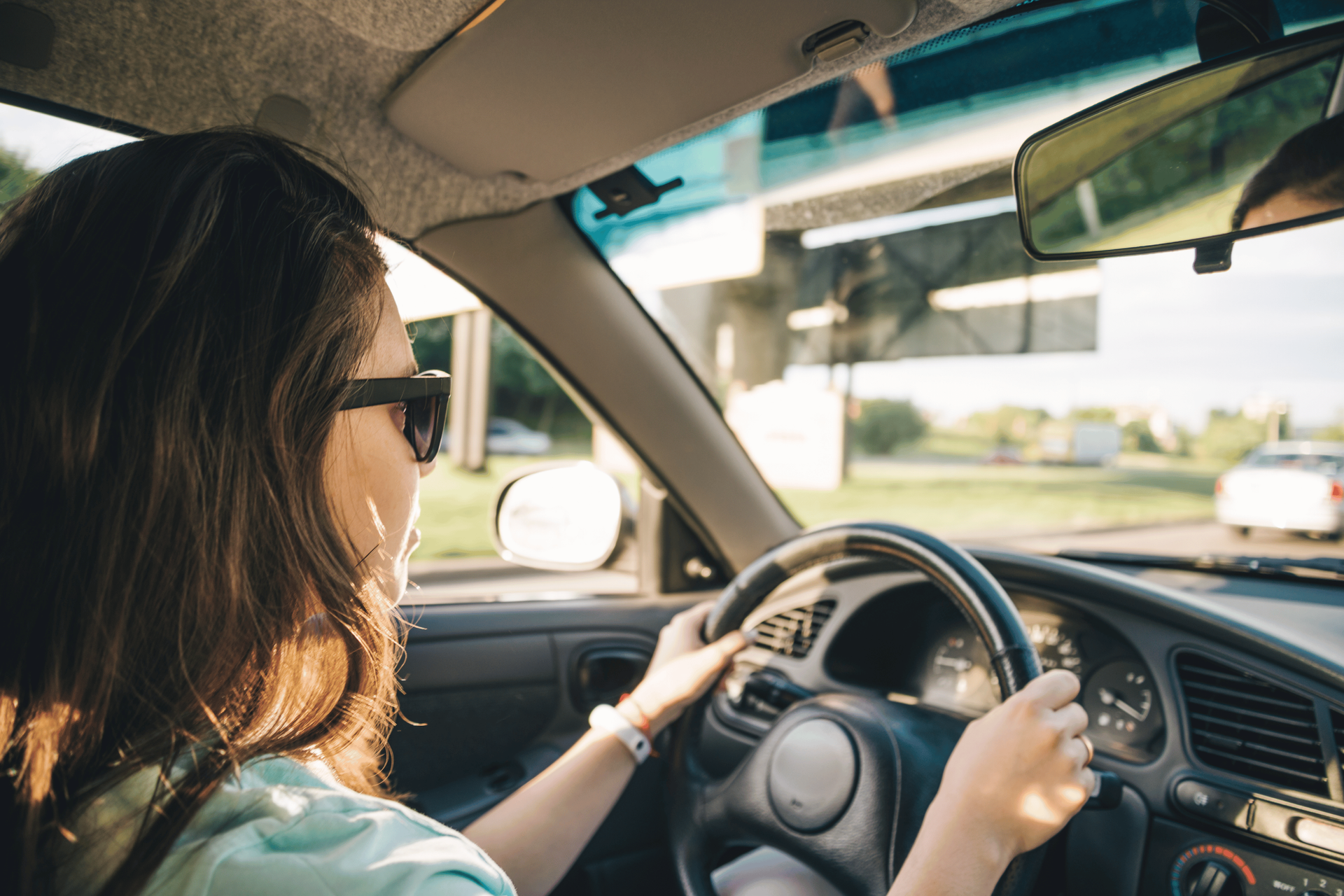 Person driving a car, seen from the back seat, with sunlight through the windshield.