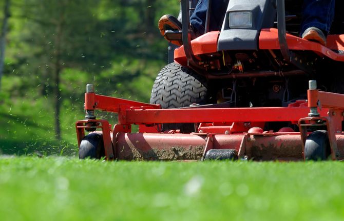 Red riding lawn mower cutting grass on a green lawn, close-up low angle