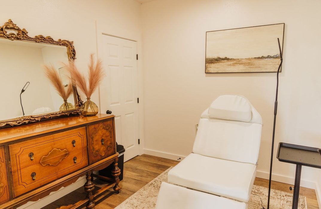 A room with a chair , dresser , mirror and painting on the wall.
