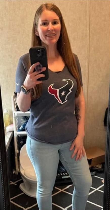 A woman in a texans shirt is taking a selfie in front of a mirror.
