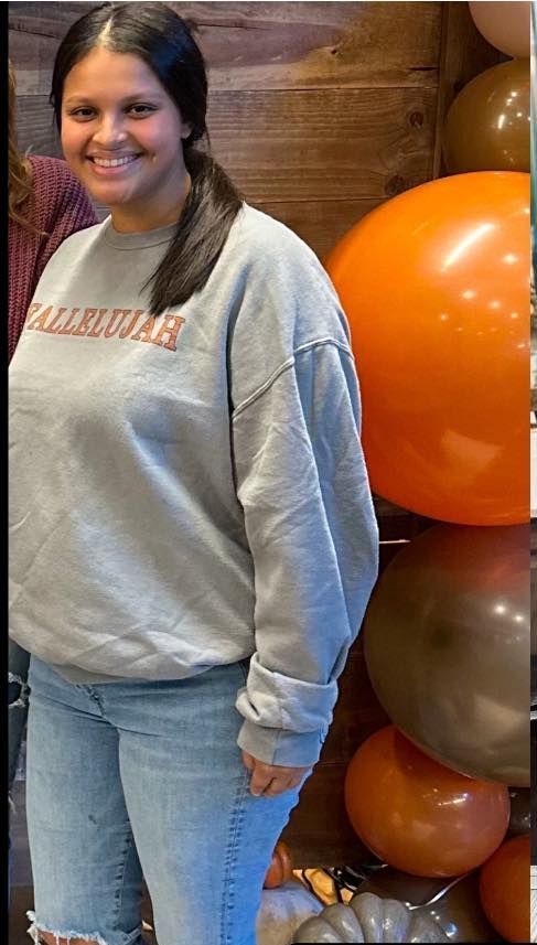 A woman in a grey sweatshirt is standing in front of balloons.