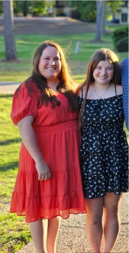 Two women in dresses are standing next to each other in a park.