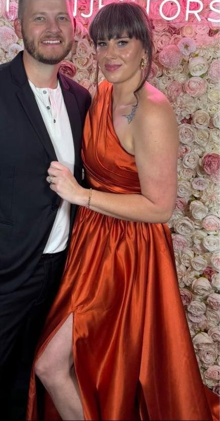 A man and a woman are posing for a picture in front of a wall of flowers.