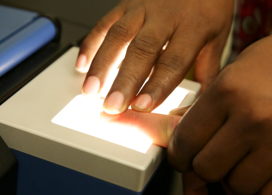 Hands using a fingerprint scanner, fingers pressed on a lit surface.