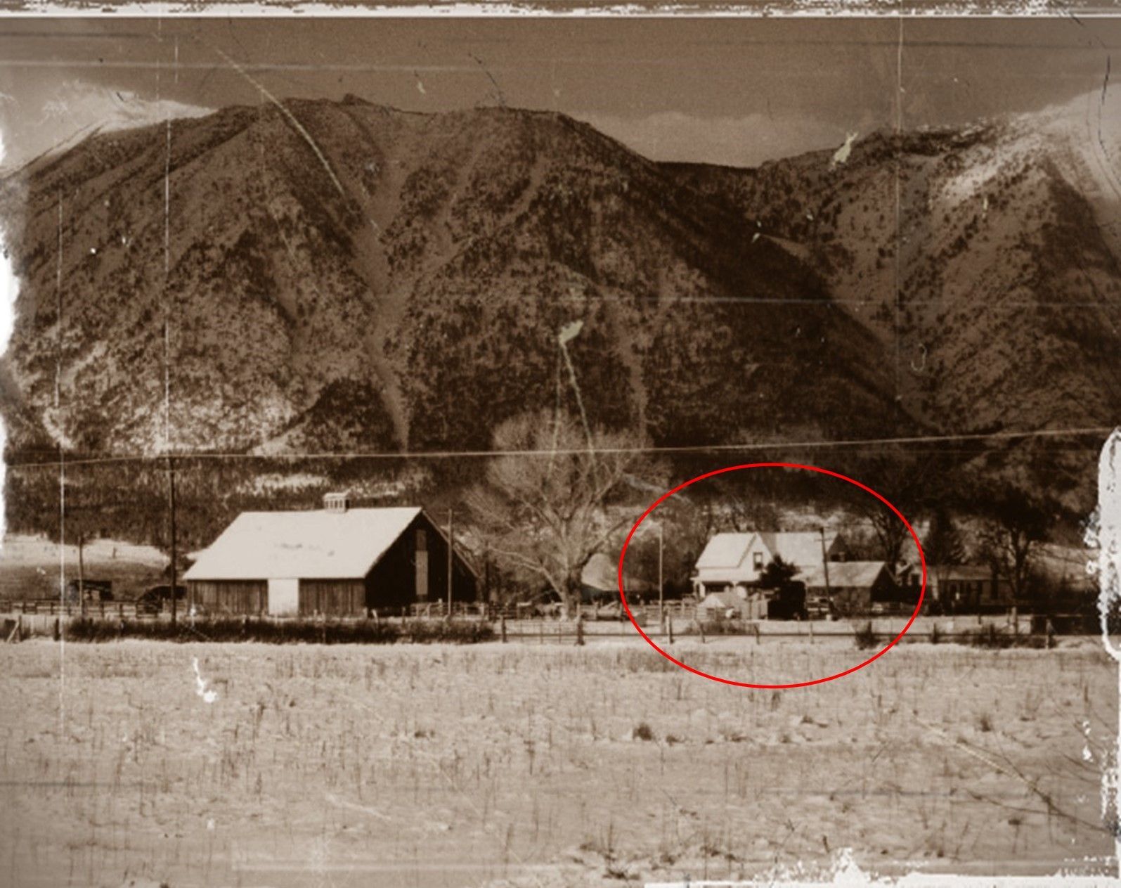 A black and white photo of a farm with mountains in the background