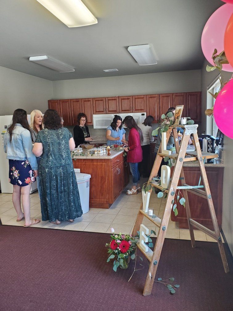 A group of women are standing in a kitchen talking to each other.