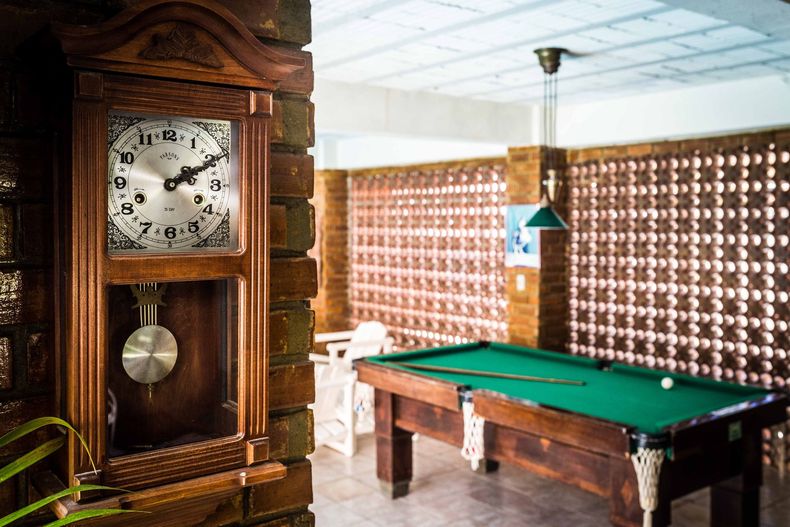 Sala de jogos revestida de madeira, com uma mesa de bilhar e um grande relógio antigo