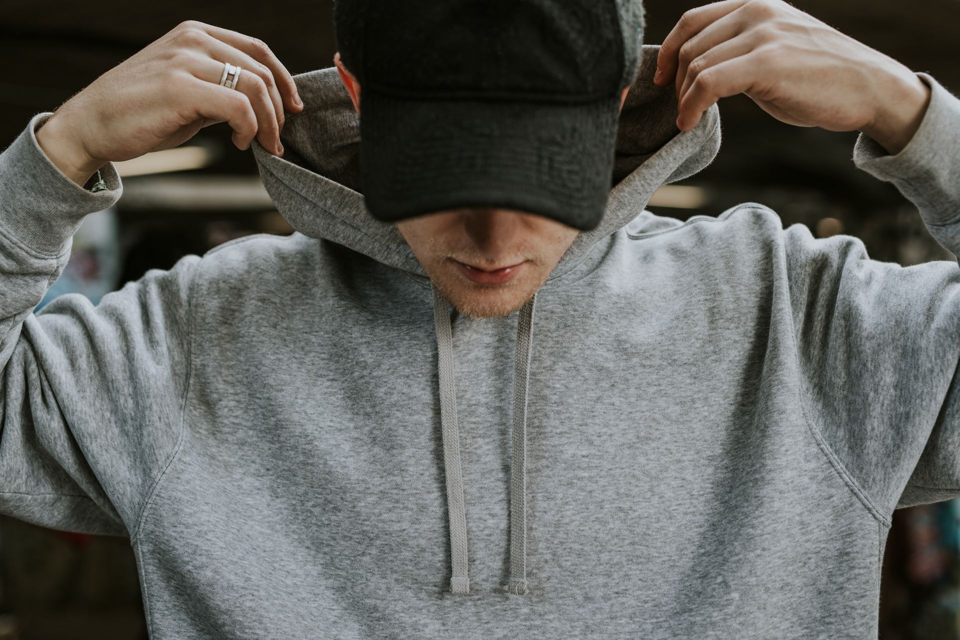 Person in a gray hoodie pulling up the hood over a black cap.