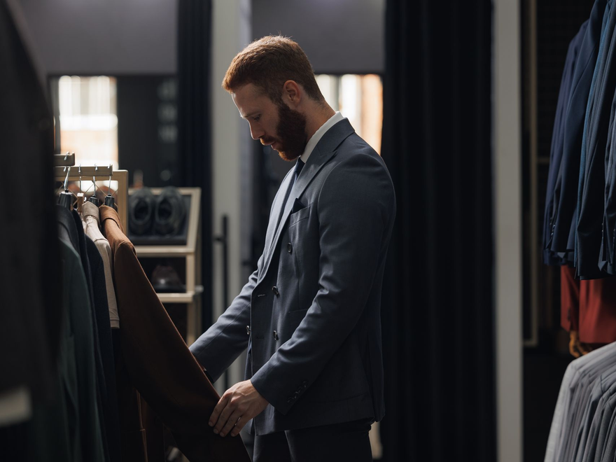 Man in a suit browsing clothes in a dimly lit boutique dressing room