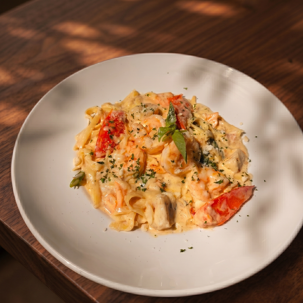 A plate of creamy shrimp and lobster pasta with herbs on a wooden table, illuminated by sunlight filtering through leaves.
