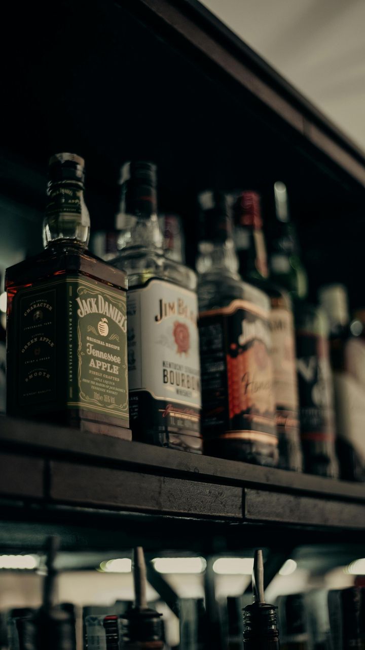 A shelf displaying various bottles of liquor, including Jack Daniel’s Tennessee Apple and Jim Beam bourbon.