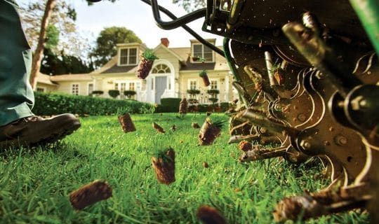 A person is using a machine to aerate their lawn in front of a house.