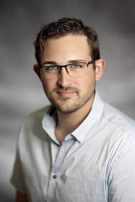 Portrait of a man in glasses and a white shirt against a blurred gray studio background