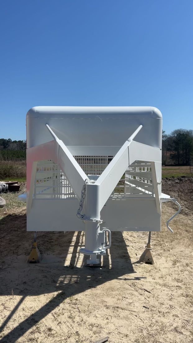 White front-view industrial machine with two angled arms on a dirt lot under a blue sky
