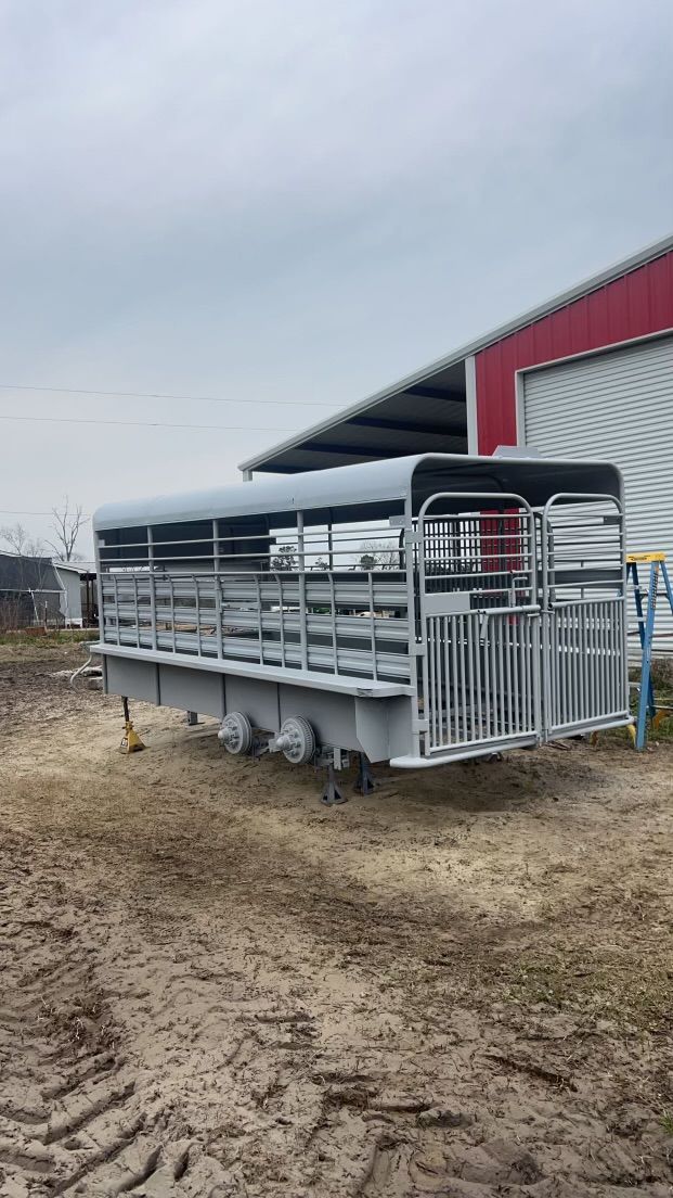 Silver livestock trailer parked beside a red barn on a muddy farm lot under an overcast sky