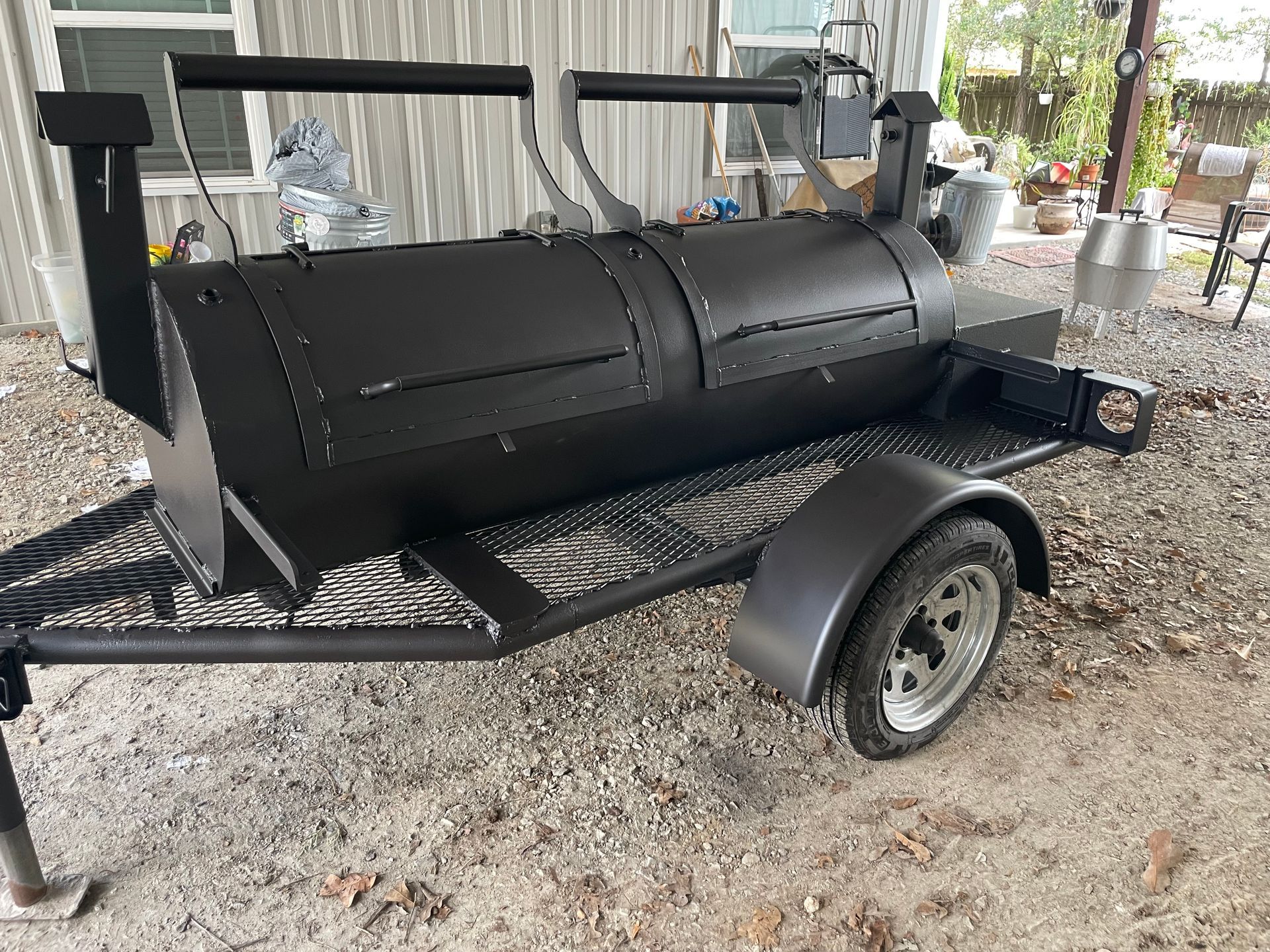 Black barrel smoker grill on a trailer under a covered outdoor area.