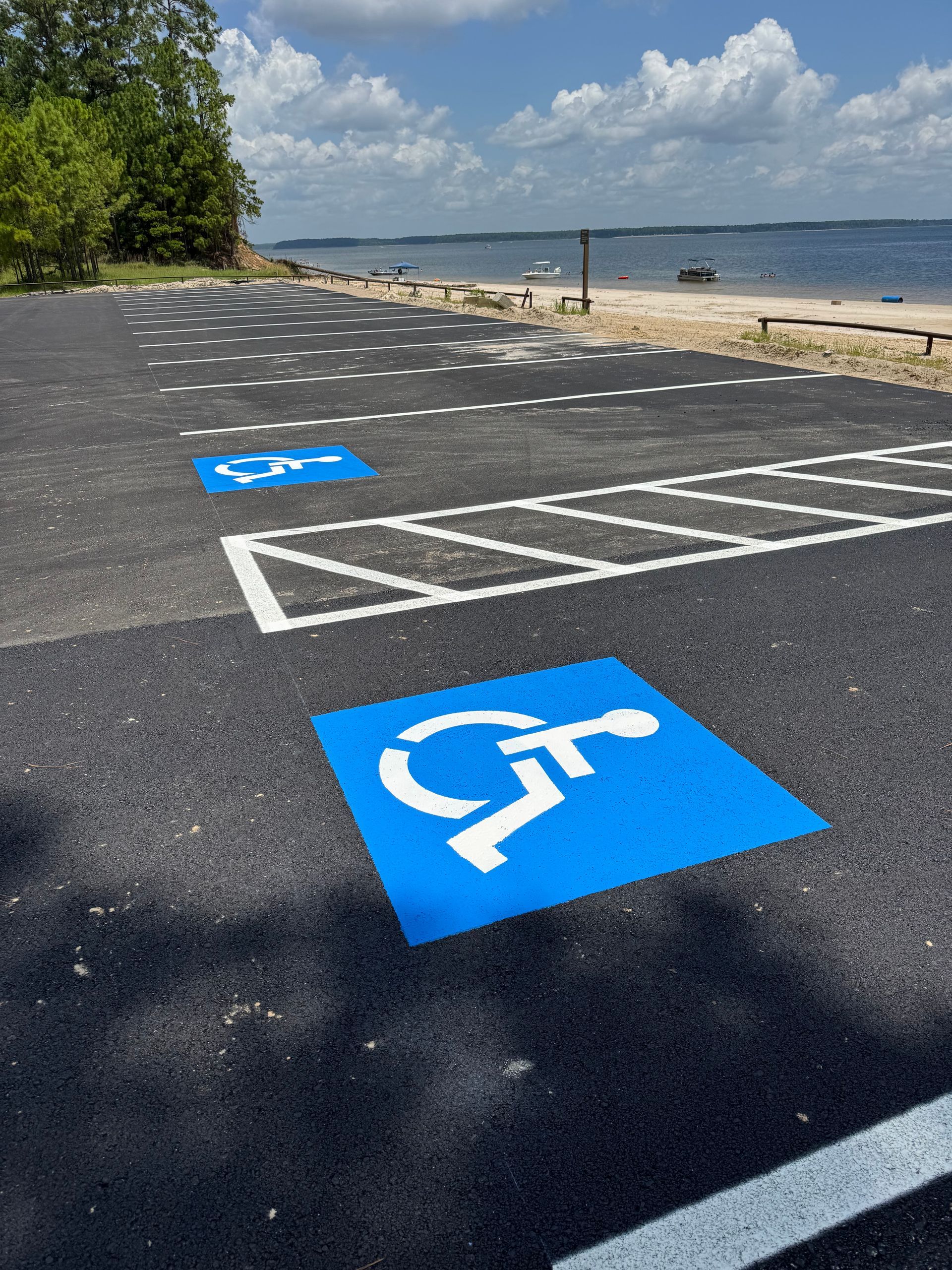 Accessible parking spaces marked with blue wheelchair symbols beside a beach and water.