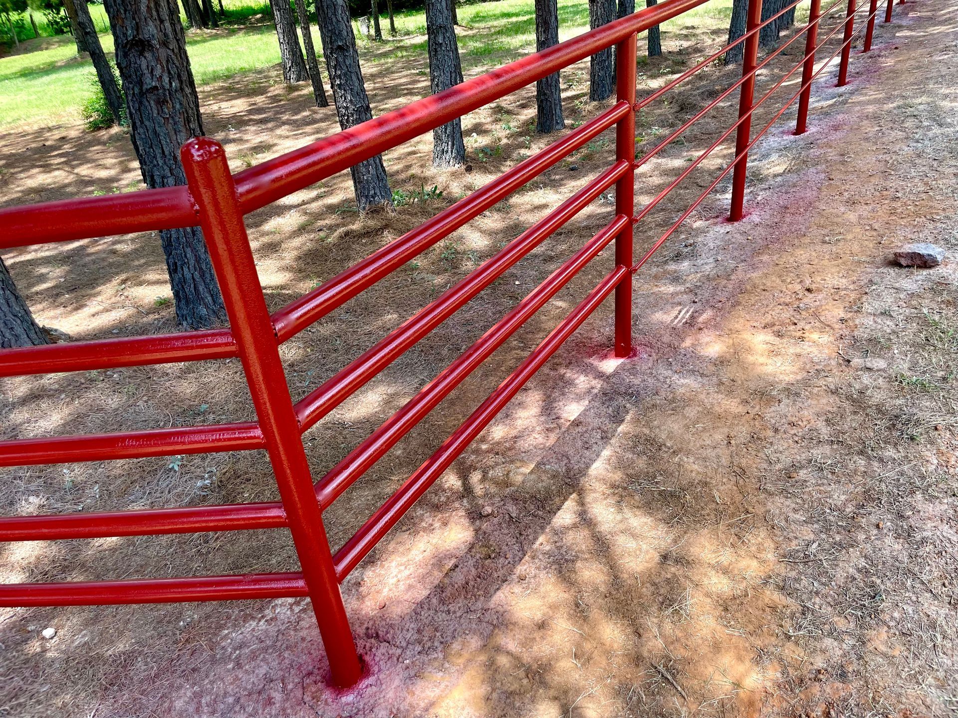 Red metal fence lining a gravel path in a wooded area