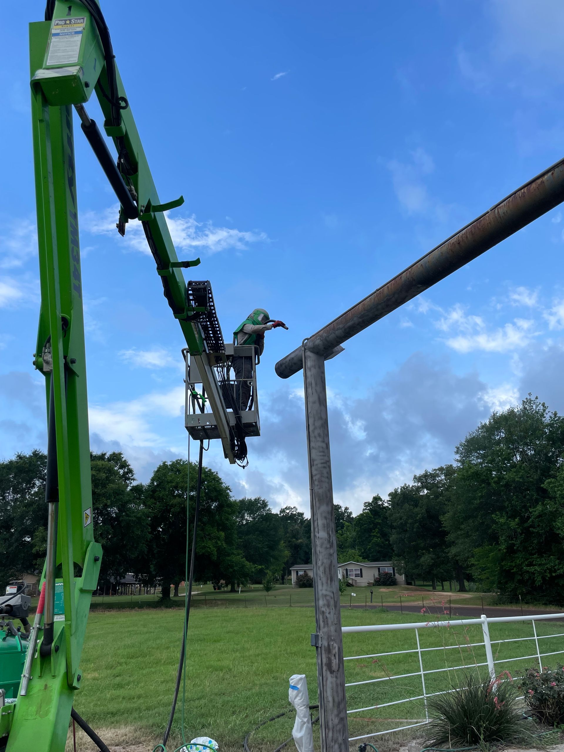 Green construction boom lift beside a wooden post in a grassy field under blue sky