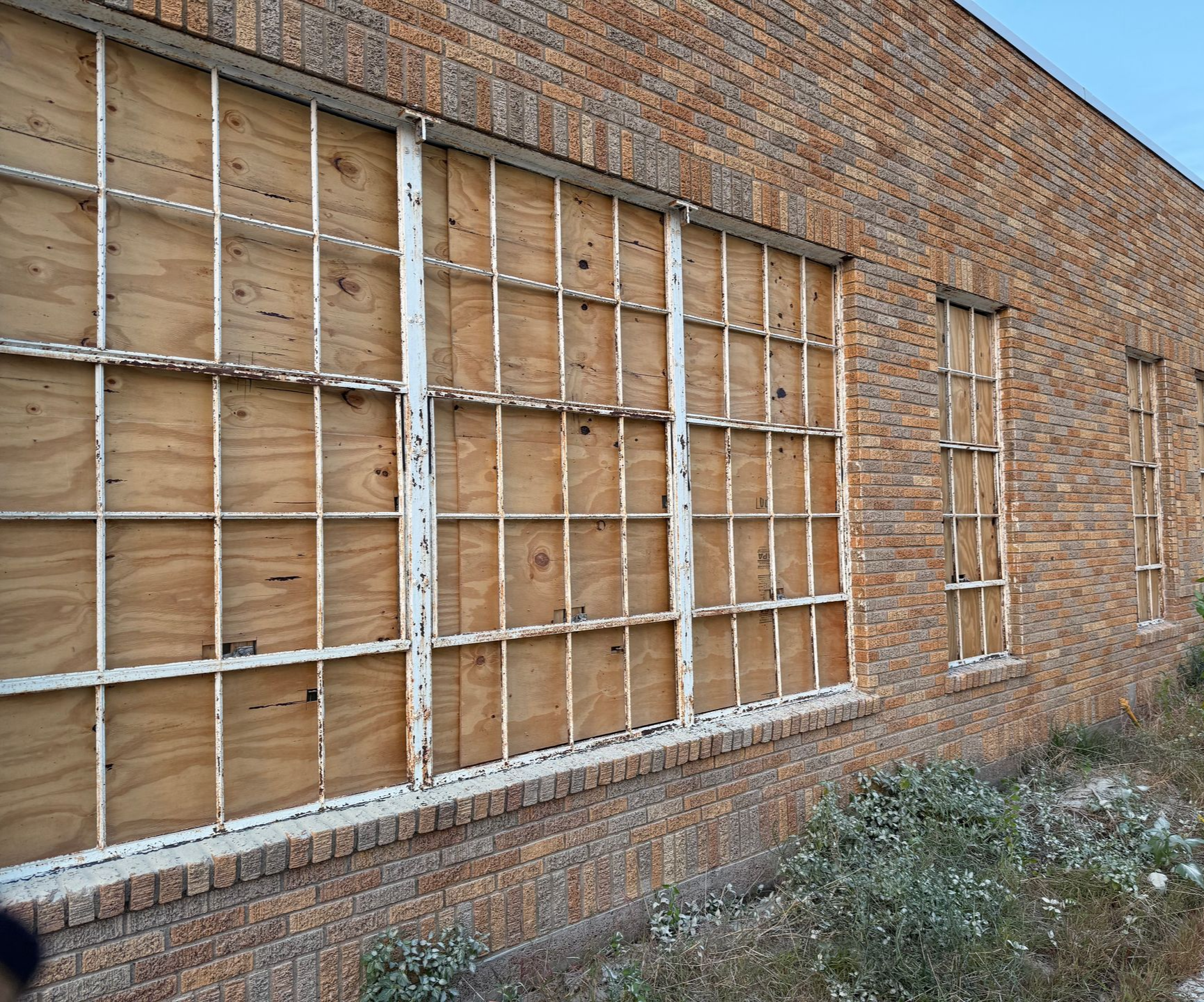 Brick building wall with boarded-up windows and metal security grates.