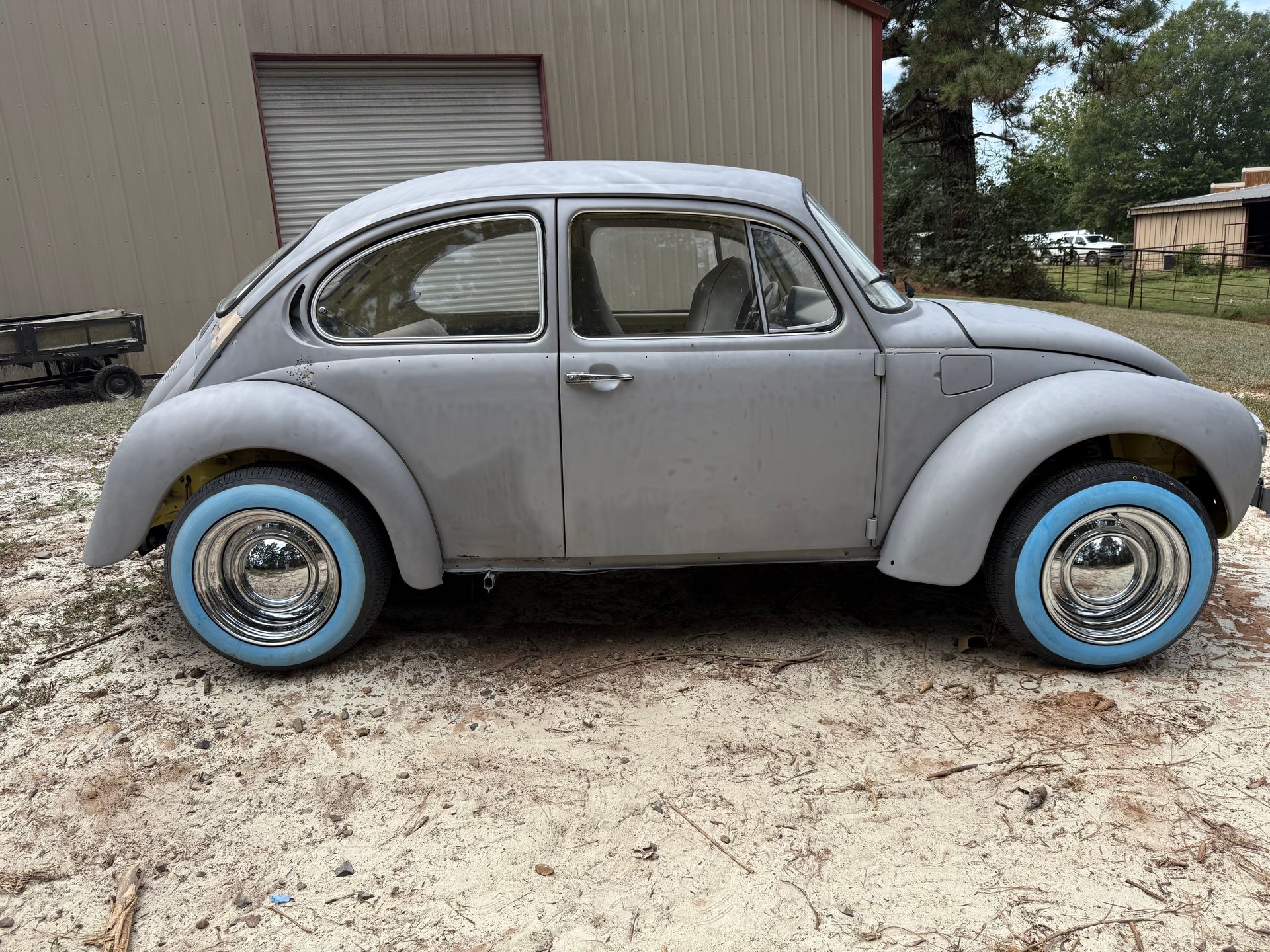 Gray vintage Volkswagen Beetle with blue wheels parked outdoors in front of a building