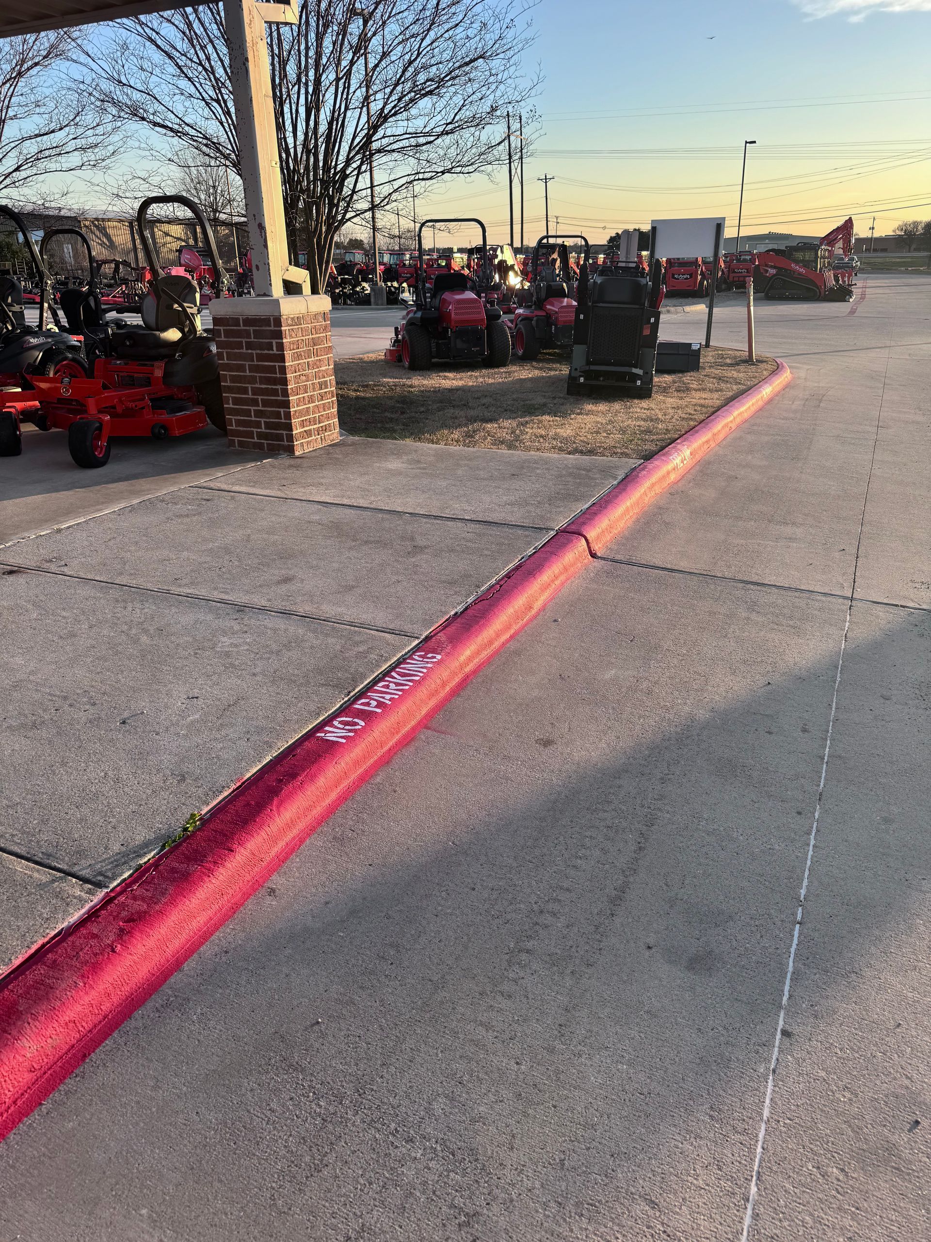 Red ride-on lawn mowers parked beside a sidewalk at sunset.
