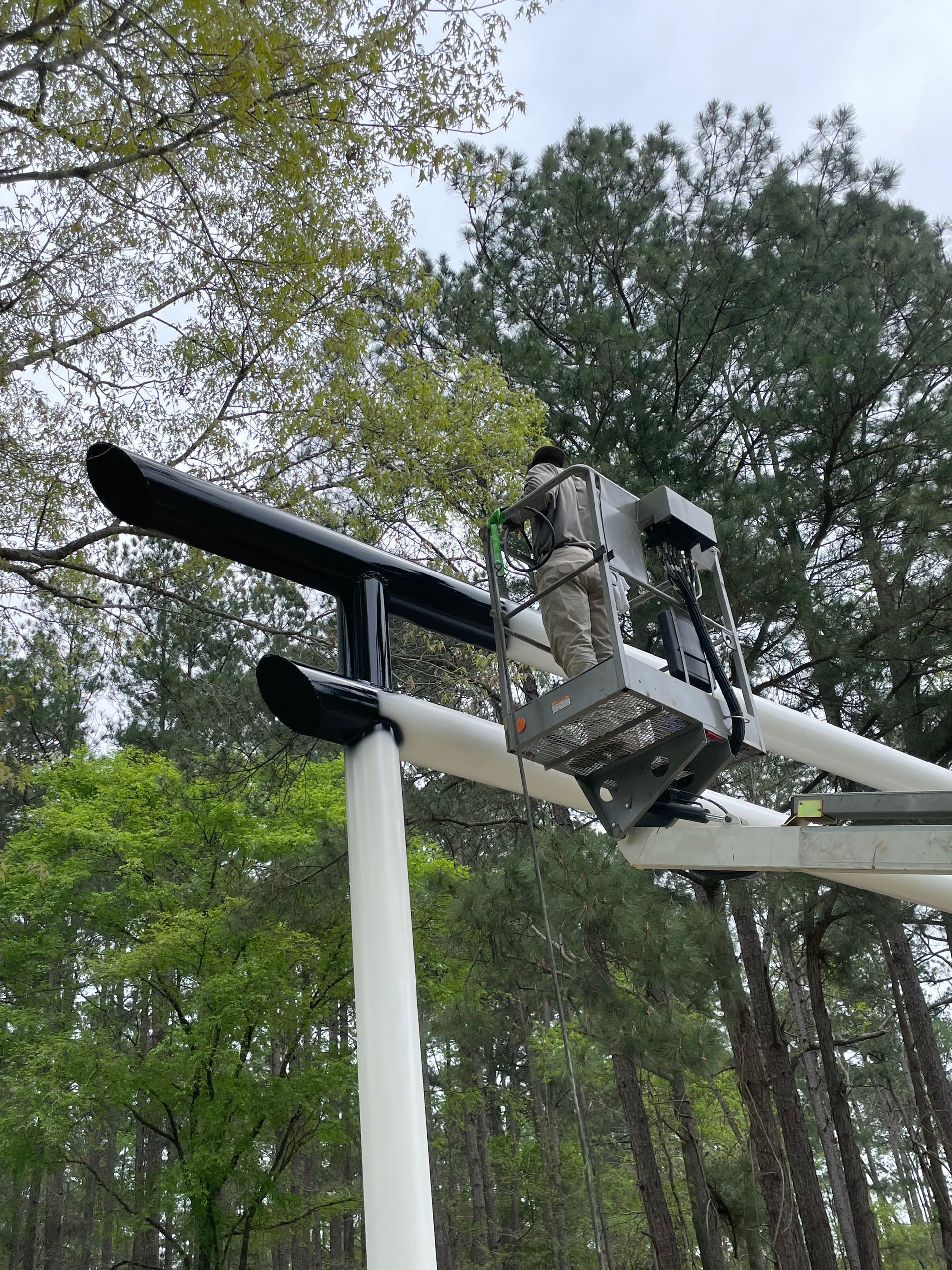 Aircraft wing seen from below among trees, with mounted equipment on the wing.