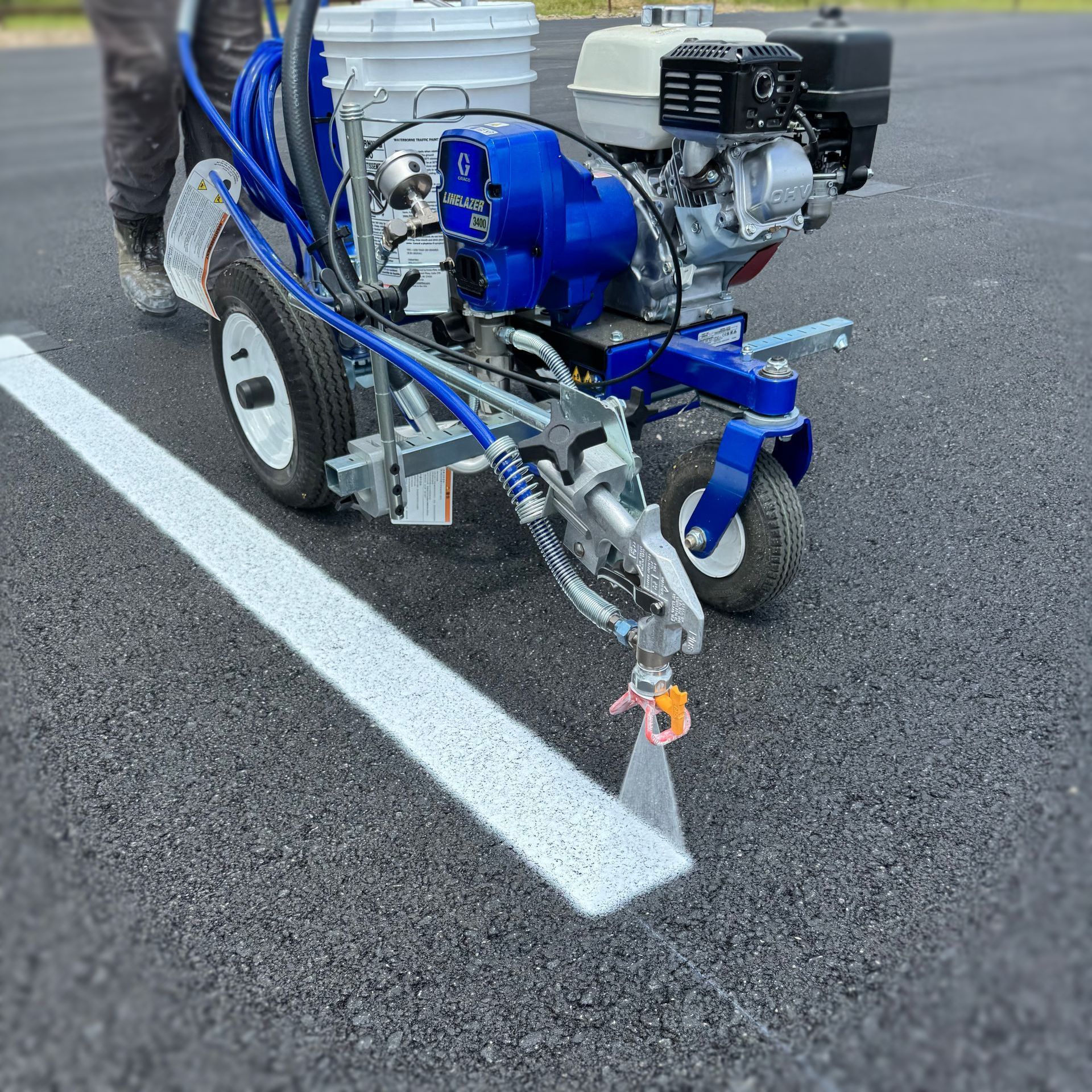 Blue line-striping machine painting a white line on asphalt pavement