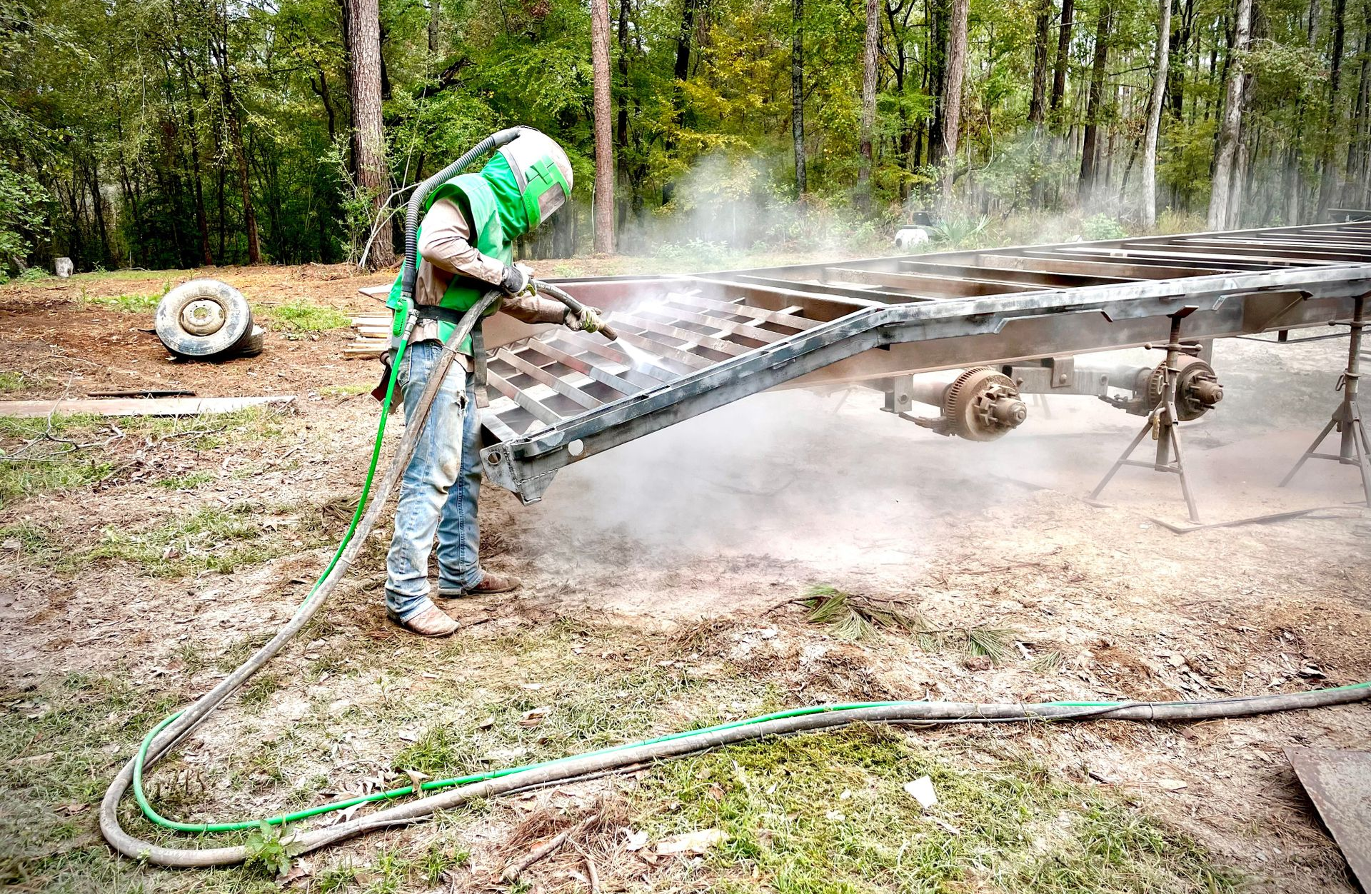 Worker in green safety gear spraying water on a smoky metal frame outdoors